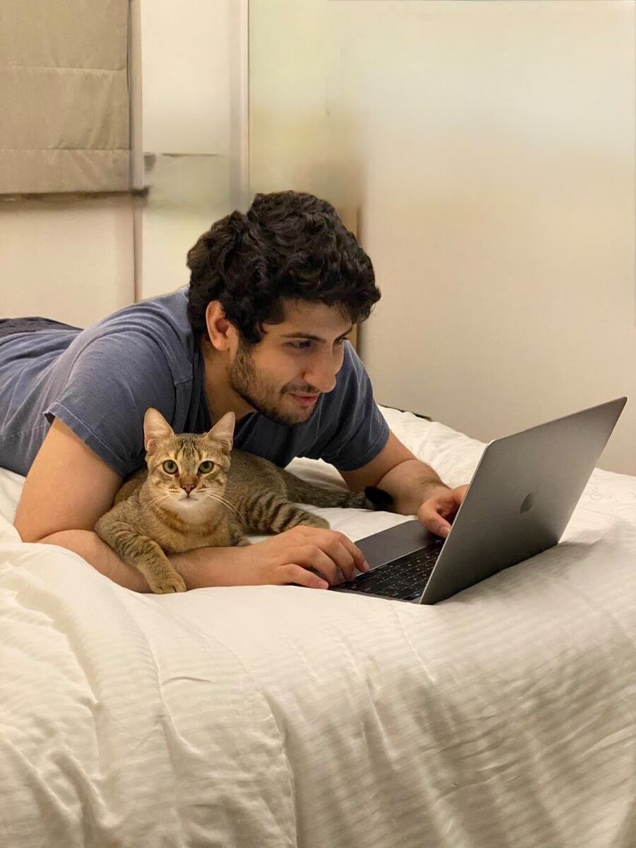 Mishal Govani working on his laptop with a tabby cat lying beside him