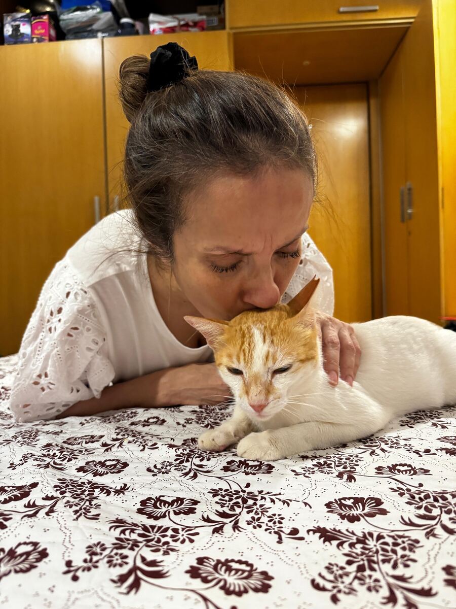 Sausan kissing the head of an orange and white rescued cat resting on a bed