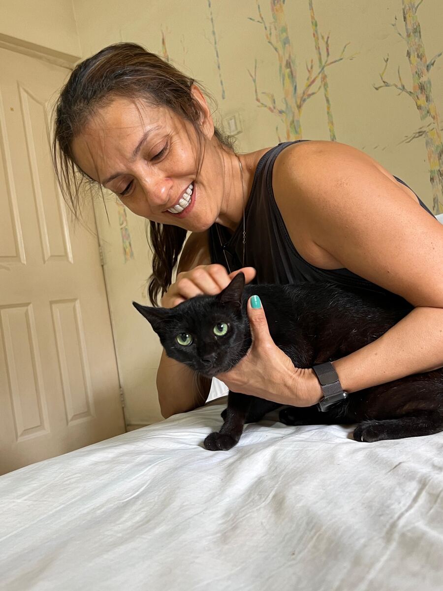 Sausan smiling as she holds a green-eyed black cat on a bed
