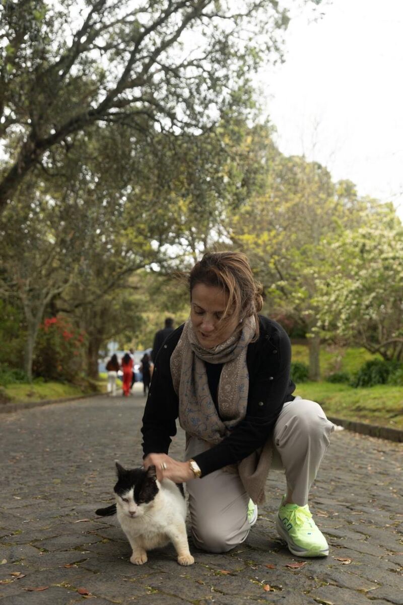 Sausan kneeling on a tree-lined path to stroke a black and white cat